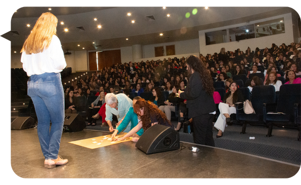 Bárbara Contreras de espaldas frente a un auditorio lleno, con personas organizando materiales en el escenario.