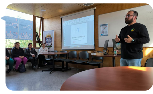 Óscar Alarcón dando una charla sobre prevención de adicciones frente a un grupo de personas en un aula, con una presentación proyectada en pantalla.