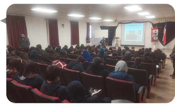 Óscar Alarcón ofreciendo una charla sobre prevención de adicciones a un grupo de estudiantes en un auditorio.