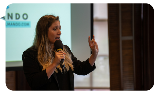 Giancarla Marisio hablando con pasión mientras sostiene un micrófono, en una conferencia profesional con una presentación proyectada de fondo.